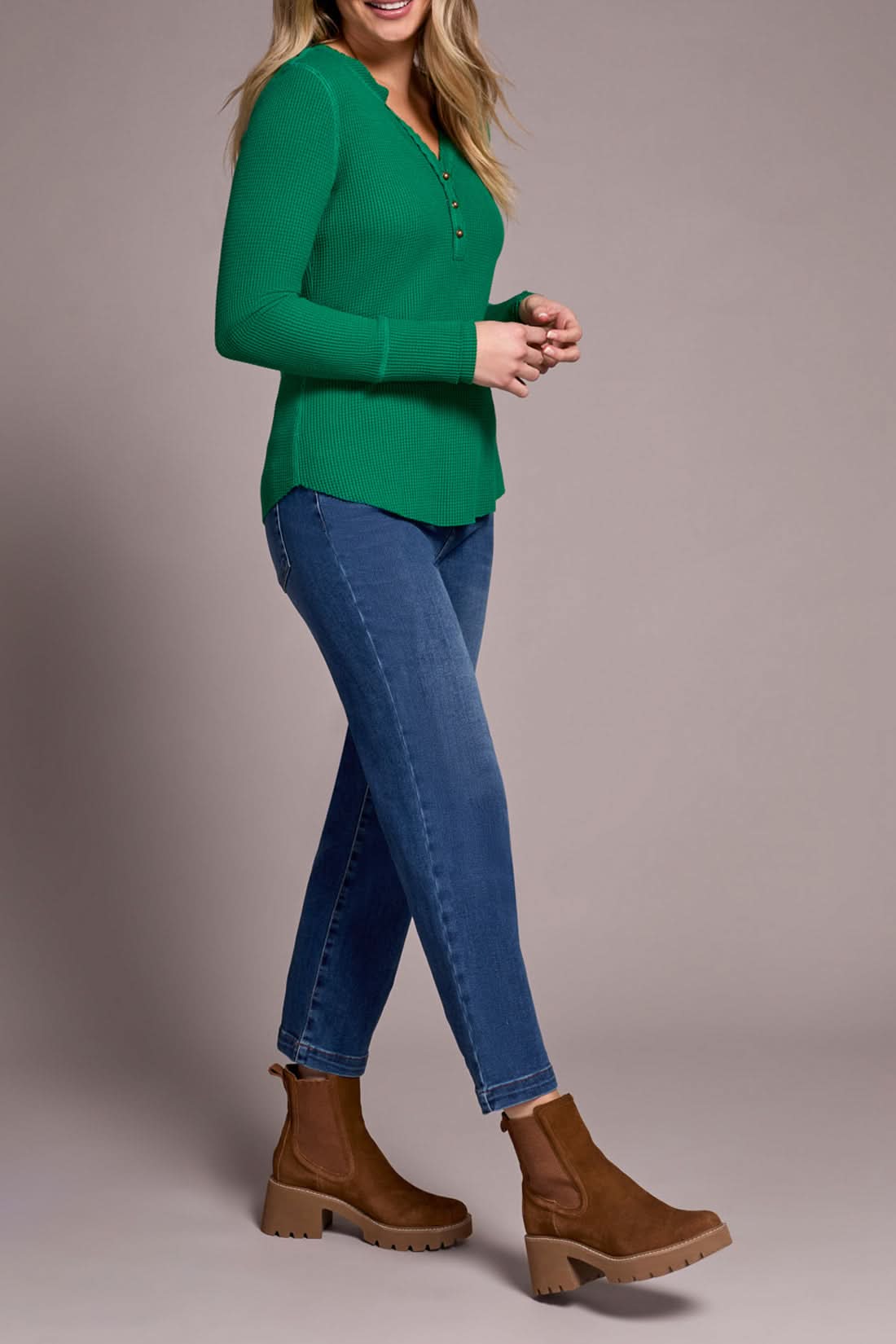 A woman indoors wears the Tribal HENLEY TOP in light blue with matching pants and beige ankle boots, standing by a cream sofa and a plant, embodying a chic, versatile style.