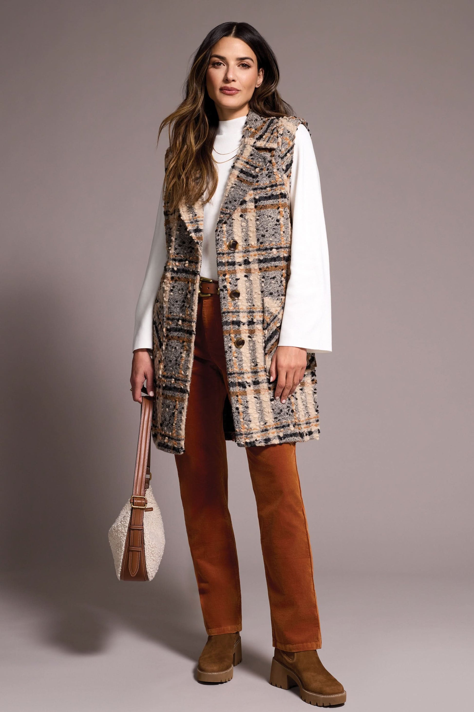 A woman models the Tribal WIDE NOTCH COLLAR VEST—a plaid, sleeveless coat with a wide notch collar—layered over a white turtleneck, rust pants, and brown boots while holding a handbag against a plain background.