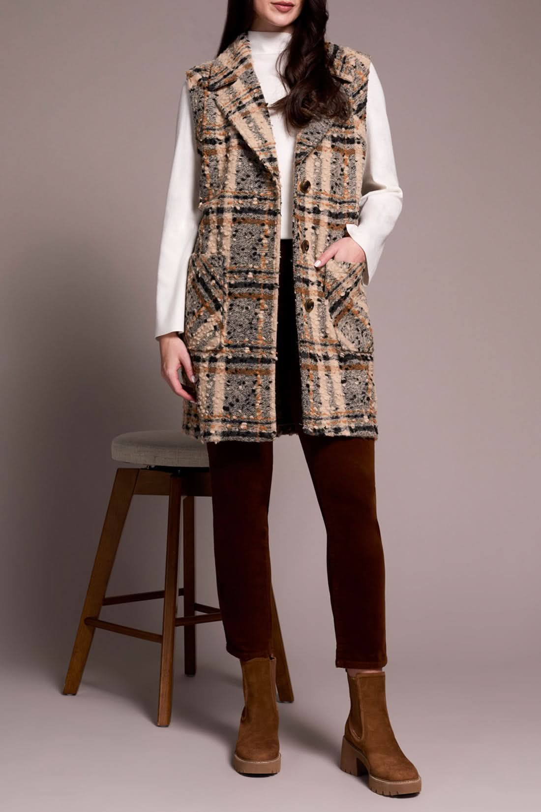 A woman models the Tribal WIDE NOTCH COLLAR VEST—a plaid, sleeveless coat with a wide notch collar—layered over a white turtleneck, rust pants, and brown boots while holding a handbag against a plain background.