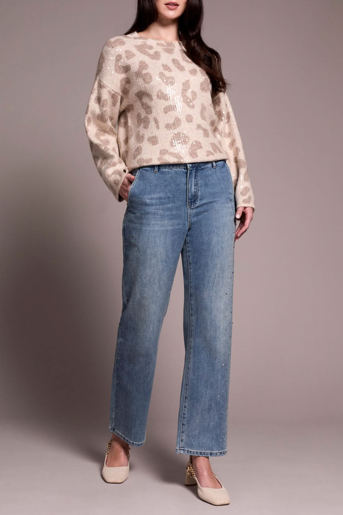 A person wearing a beige leopard-print sweater, Tribal’s BROOKE SUPER STRAIGHT W/ STONES light blue pants for a comfortable fit, and cream heels stands against a plain background.