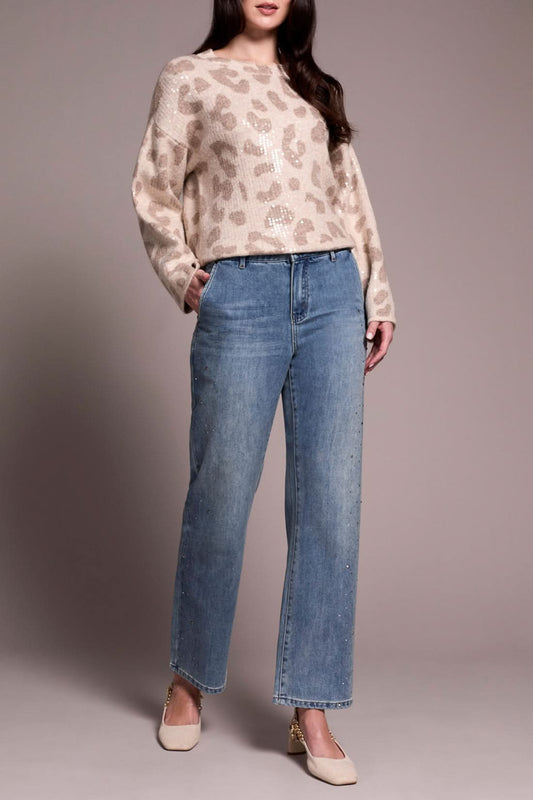 A person wearing a beige leopard-print sweater, Tribal’s BROOKE SUPER STRAIGHT W/ STONES light blue pants for a comfortable fit, and cream heels stands against a plain background.