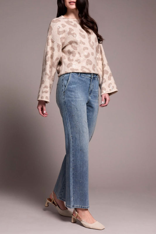 A person wearing a beige leopard-print sweater, Tribal’s BROOKE SUPER STRAIGHT W/ STONES light blue pants for a comfortable fit, and cream heels stands against a plain background.