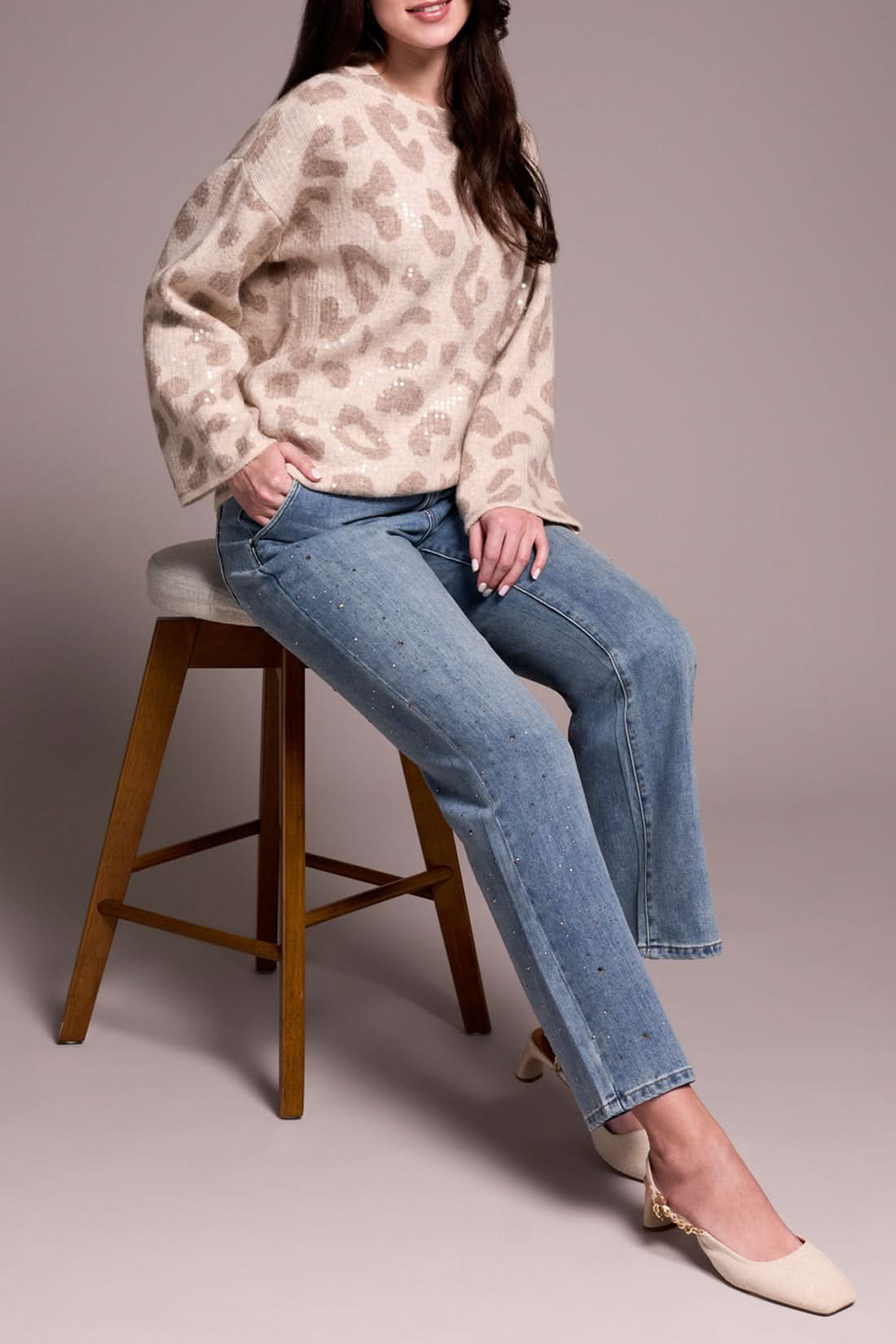 A person wearing a beige leopard-print sweater, Tribal’s BROOKE SUPER STRAIGHT W/ STONES light blue pants for a comfortable fit, and cream heels stands against a plain background.