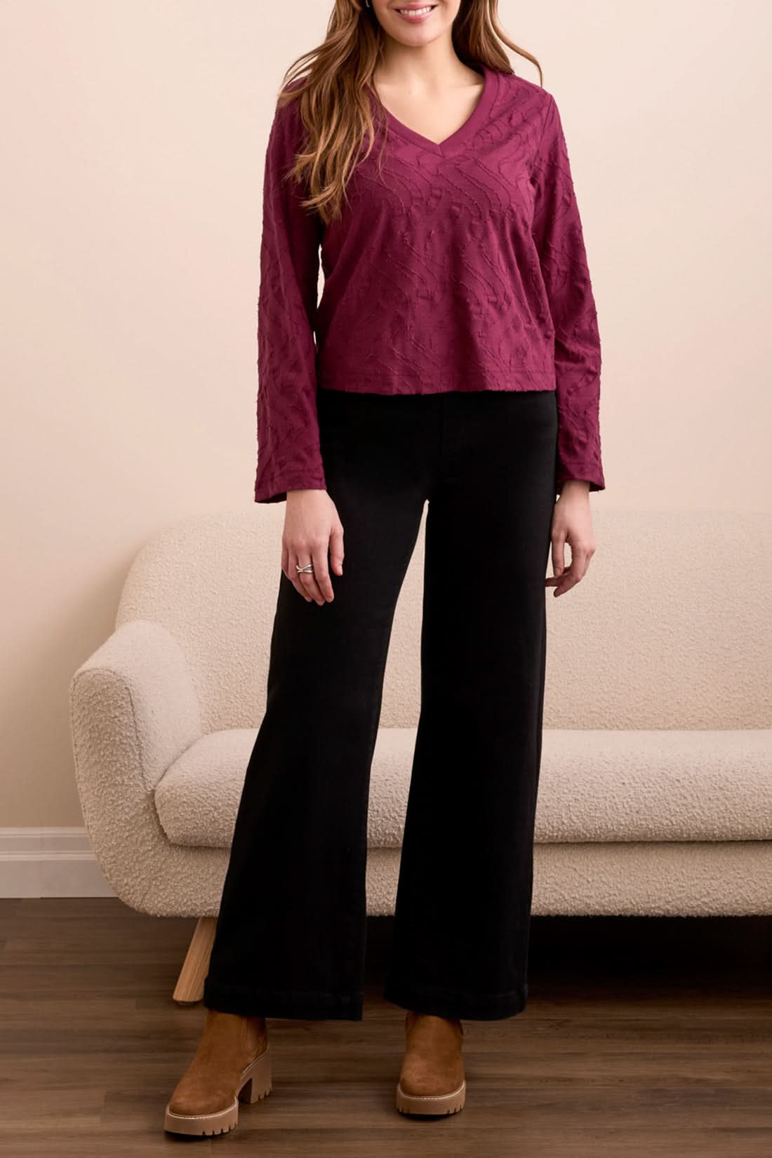 A woman stands indoors wearing the Tribal V NECK TOP in wine, paired with black wide-leg pants and brown platform shoes, with a beige couch in the background.