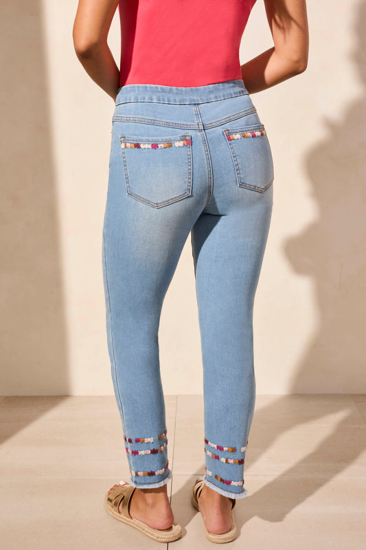 A woman stands against a beige wall wearing a sleeveless coral top, Tribal AUDREY PULL ON SLIM ANKLE JEANS with beaded hems for a flattering fit, and beige sandals—blending comfort and effortless style.