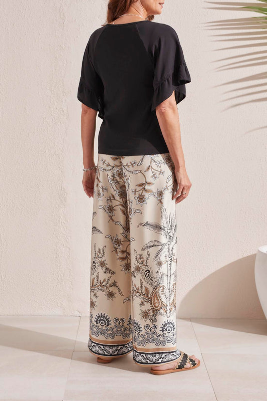 Woman smiling, wearing a black Tribal V Neck Raglan Combo Sleeved Top with a floral print skirt.