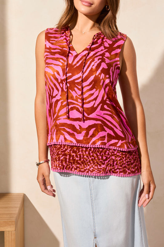 A woman wears the Tribal Sleeveless Combo Print Blouse, featuring a cute pink and orange tiger stripe design with a hood, paired with a light-wash denim skirt for a fun look.
