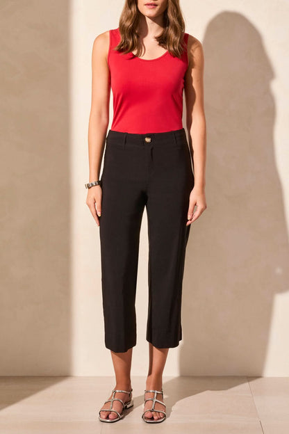 A person in a red sleeveless top, FLOWY HIGH RISE TWILL CAPRI PANT by Tribal, and sandals stands in a well-lit room with light-colored walls and floor, facing away.