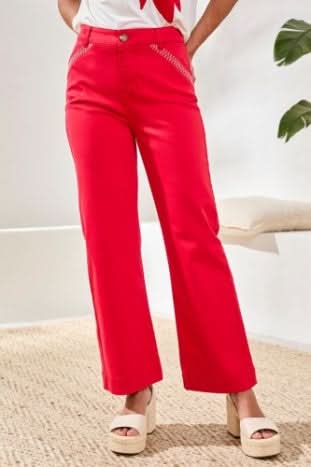 A person wearing Tribal’s Fly Front Ankle Pant with embroidery detail, featuring bright pink fabric, white zigzag stitching near the pockets, and a brown waistband button.