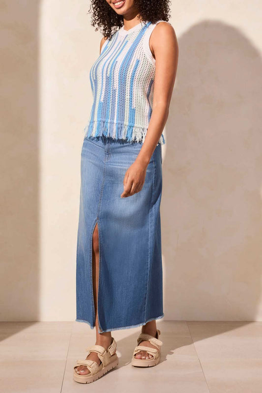 A person faces away, wearing the Tribal CREW NECK FRINGED HEM SWEATER with blue and white stripes, paired with a long light blue denim skirt and beige shoes.