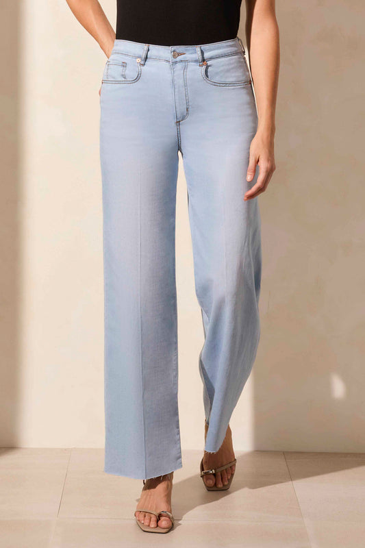 A person is shown from the waist down in natural light wearing Tribal’s BROOKE HUGGING WIDE TROUSER JEANS in light blue with a black sleeveless top.