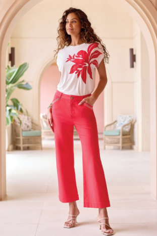 A person wearing Tribal’s Fly Front Ankle Pant with embroidery detail, featuring bright pink fabric, white zigzag stitching near the pockets, and a brown waistband button.