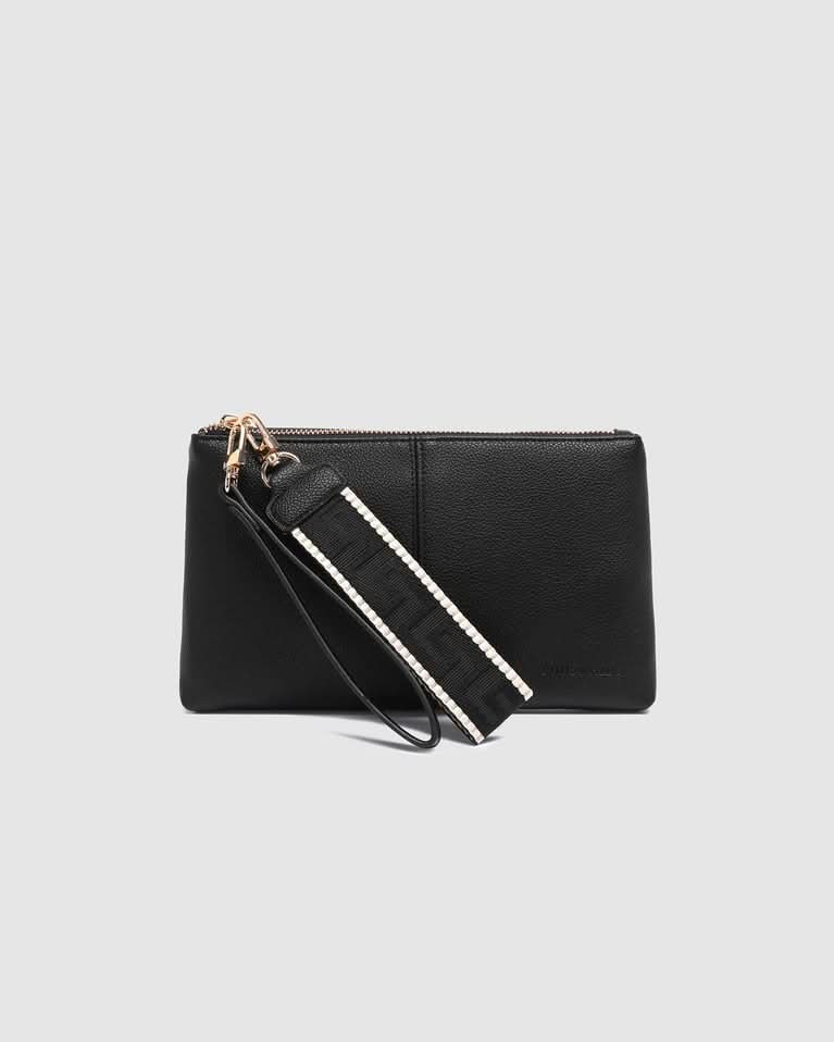 A person in white pants holds the Louenhide Mimi Gia Wristlet, a vegan leather accessory with a thick strap—an everyday essential for style and convenience, pictured standing indoors on steps.