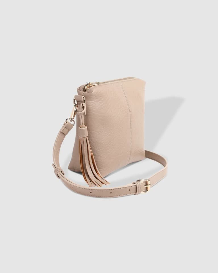 A person in a striped sleeveless top and pleated skirt carries the Louenhide Kasey Textured Crossbody Bag, featuring a wide strap and tassel.